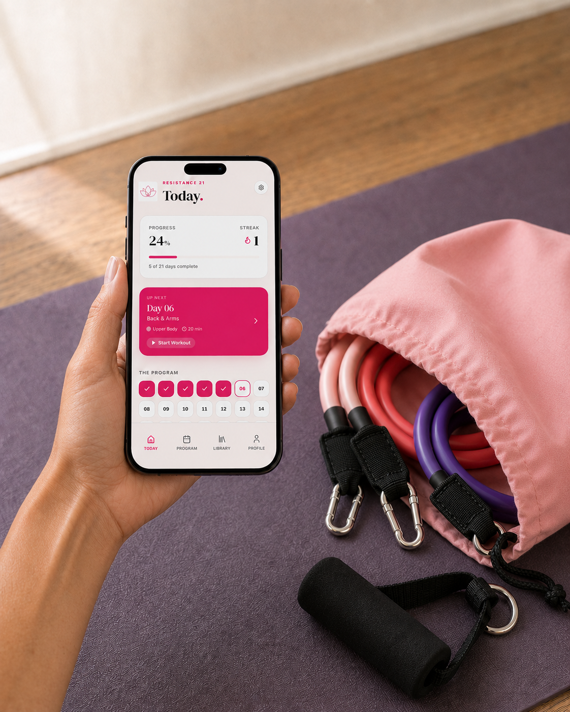 Movita resistance bands and blush-pink pouch beside a phone showing the Resistance21 workout plan.